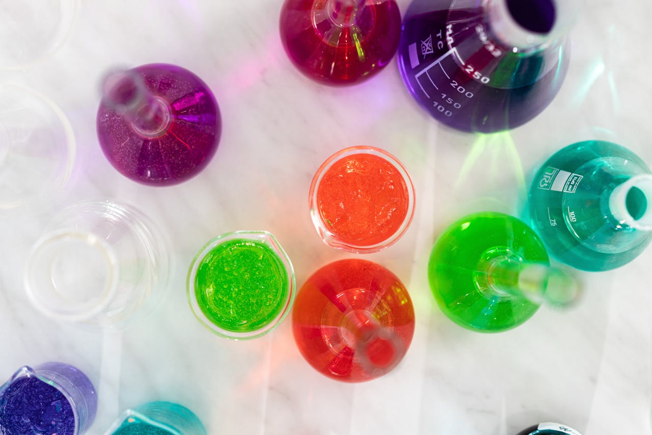 Aerial view of colorful liquids in laboratory glassware on marble surface, showcasing vibrant hues.